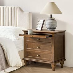 a nightstand with a lamp on top of it next to a bed