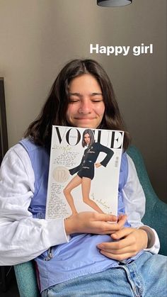 a woman sitting in a chair holding up a magazine with an image of a model on it