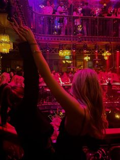 a woman reaching up into the air in front of a group of people at a bar