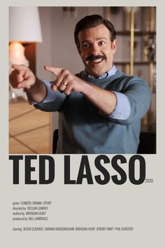 a man pointing his finger at the camera in front of a poster that says ted lasso