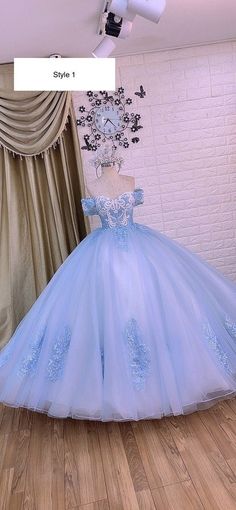 a blue ball gown is on display in front of a white brick wall and wooden floor