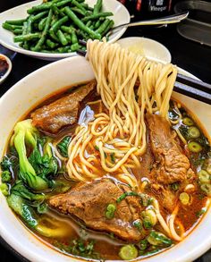 a bowl filled with noodles, meat and veggies on top of a table