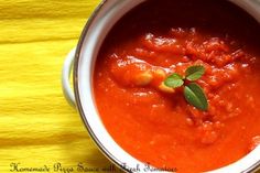 a white bowl filled with red sauce on top of a yellow table cloth and green leafy garnish