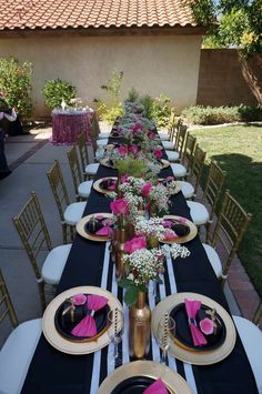 the table is set with black and white linens, pink napkins, and gold chargers