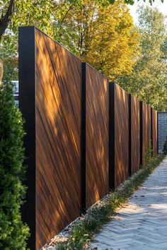 a long wooden fence next to a sidewalk in the middle of some trees and bushes