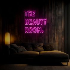 a neon sign that says the beauty room in front of a couch with pillows on it