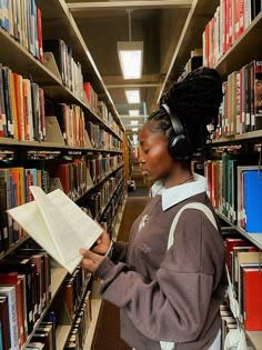 a woman reading a book in a library with headphones on her ears and listening to music