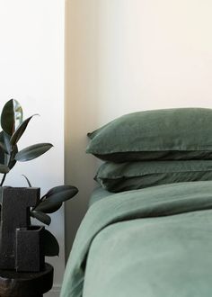 a bed with green sheets and pillows next to a potted plant