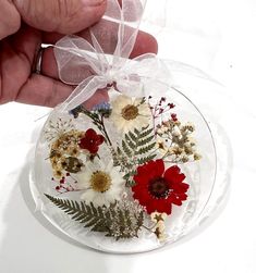 a hand holding a clear glass ornament with flowers and greenery in it