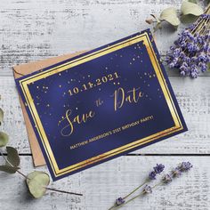 a blue and gold save the date card on top of a wooden table with purple flowers