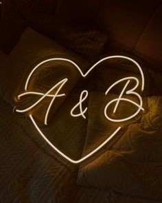 a heart shaped neon sign sitting on top of a bed