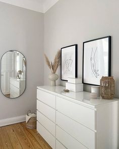 a white dresser with two framed pictures on it and a mirror above it in a room