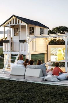 four people sitting on the back of a couch in front of a house with a tv