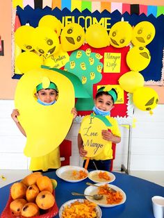 two children are holding up signs with faces on them at a table filled with food