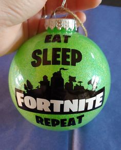 a hand holding a green ornament that says eat sleep fortnite repeat