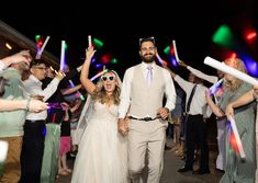 a bride and groom walking through a crowd with their arms in the air holding sparklers