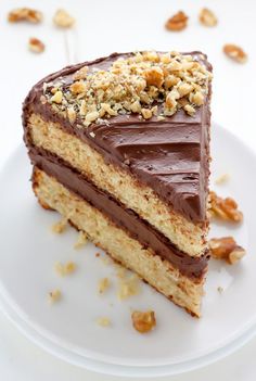 a piece of cake with chocolate frosting and walnuts on top is sitting on a white plate