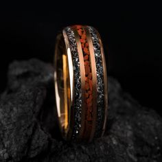 two gold and black bands with red coral inlays on top of rocks,