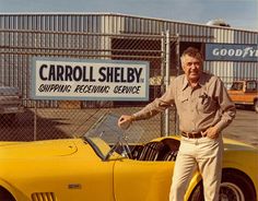 a man standing next to a yellow sports car in front of a sign that says carol sheby shipping receiving service