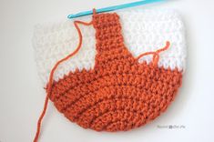 an orange and white crochet purse with a blue handled knitting needle next to it