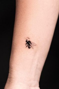 a small black and white bee tattoo on the wrist