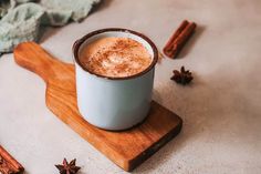 a cup of hot chocolate sitting on top of a wooden board next to cinnamon sticks