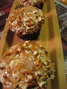 three muffins with caramel drizzled on them sitting on a wooden tray