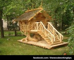 a tree house made out of logs in the grass with stairs leading up to it