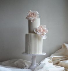 a three tiered white cake with pink flowers on the top and bottom, sitting on a bed