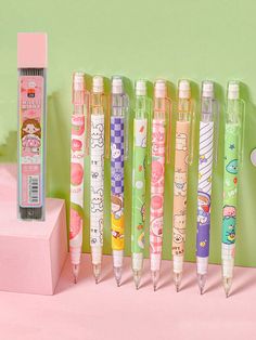 several pens lined up next to each other in front of a pink box and green wall