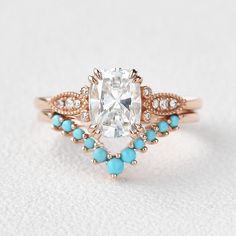 an oval cut diamond surrounded by blue turquoise stones in a rose gold band setting on a white background