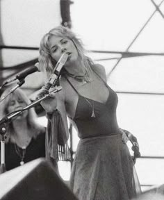 a black and white photo of a woman singing into a microphone at an outdoor concert