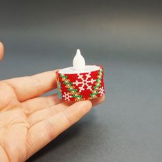 a hand holding a small red and green beaded ring with a white candle in it