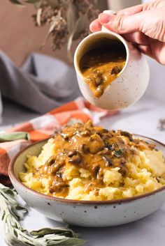 someone is pouring gravy over mashed potatoes in a bowl on a table