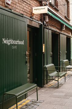 two green benches sitting on the side of a street next to tall brick buildings with windows