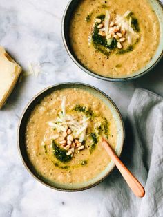 two bowls filled with soup on top of a white counter next to a wooden spoon