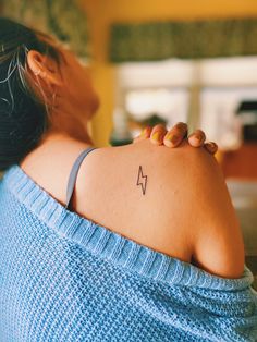 a woman with a small arrow tattoo on her upper arm and shoulder, looking down at the ground