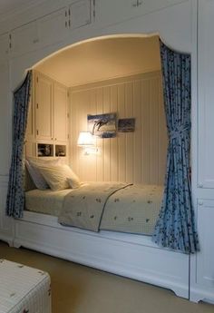 a white bed sitting under a window next to a wall mounted cabinet and night stand