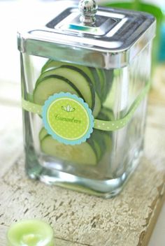 cucumber slices in a glass container sitting on a table next to a candle