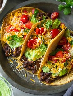 three tacos on a plate with guacamole and tomatoes