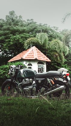 two motorcycles parked next to each other in front of a small white building with a red roof