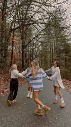 three girls are holding hands and walking down the road in front of some bare trees