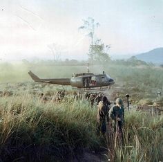 two men are standing in front of a helicopter on the side of a dirt road