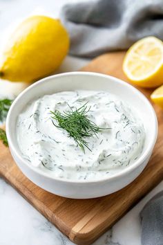 a white bowl filled with dill dip on top of a wooden cutting board next to lemons