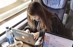 a woman sitting in front of a laptop computer on top of a desk next to a cup of coffee