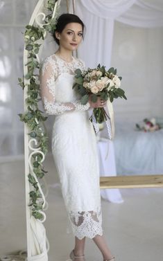 a woman in a white dress holding a bouquet and standing next to a wedding arch