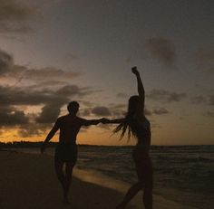 two people are running on the beach at sunset with their arms up in the air