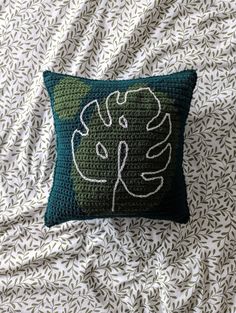 a crocheted pillow sitting on top of a bed covered in white and green leaves