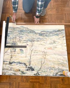 a man is painting on the floor with paintbrushes and tape as he stands next to an easel