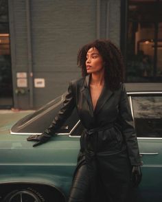 a woman leaning on the hood of a car in front of a building with an open door